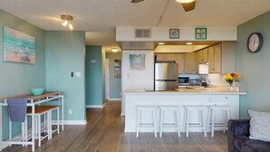 A modern kitchen with white cabinetry, a central island with stools, and a dining area with a table and chairs. - Sea Colony B7-one bedroom one bath, 1st floor, oceanfront rental located in Carolina Beach with panoramic views (Carolina Beach)