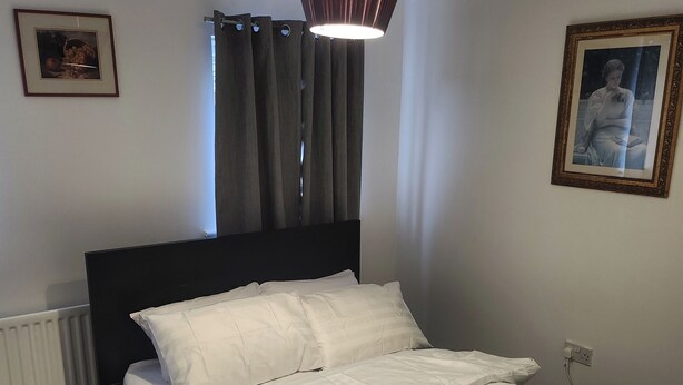 Una cama bien hecha con ropa de cama blanca, un cabecero negro y una única almohada blanca.