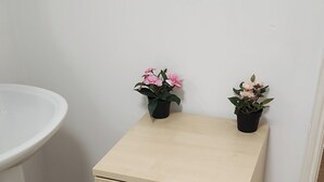 Un mueble de madera claro pequeño, con dos cajones y dos plantas en macetas encima.