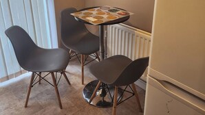 Una habitación pequeña con una mesa, cuatro sillas, un refrigerador y un radiador.