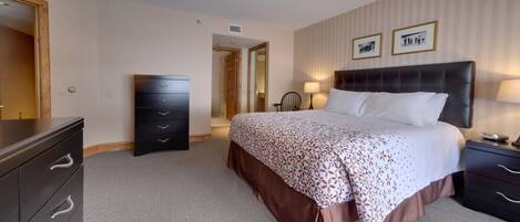 Habitación de hotel con una cama grande, una cómoda, una mesita de noche y una puerta que da a otra habitación.