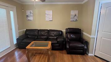 A living room with a ceiling fan, a wooden coffee table, two black leather sofas, and a door.