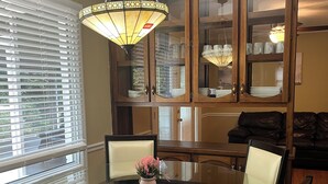 Un comedor con una mesa de vidrio rodeada de sillas, una lámpara de araña y armarios de madera con puertas de cristal.