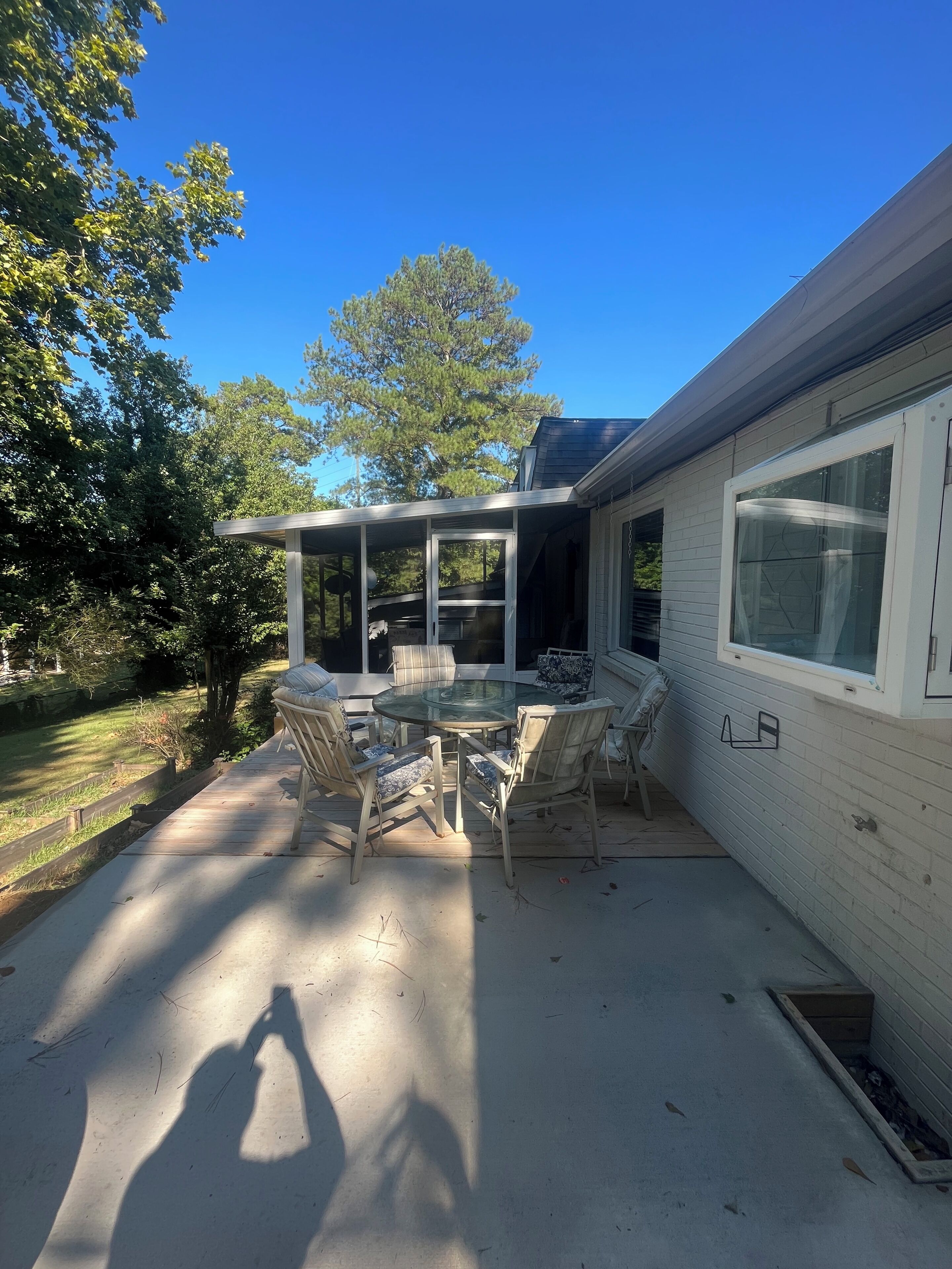 A covered patio with a glass table and chairs, a wooden deck, and a house with a window.