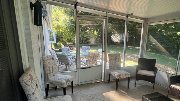 Un patio techado con puerta de vidrio que da al exterior, con una mesa y sillas, y vista al jardín trasero.