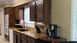 Una cocina con armarios de madera, encimera de granito, lavavajillas, cafetera y mesa de comedor de vidrio.