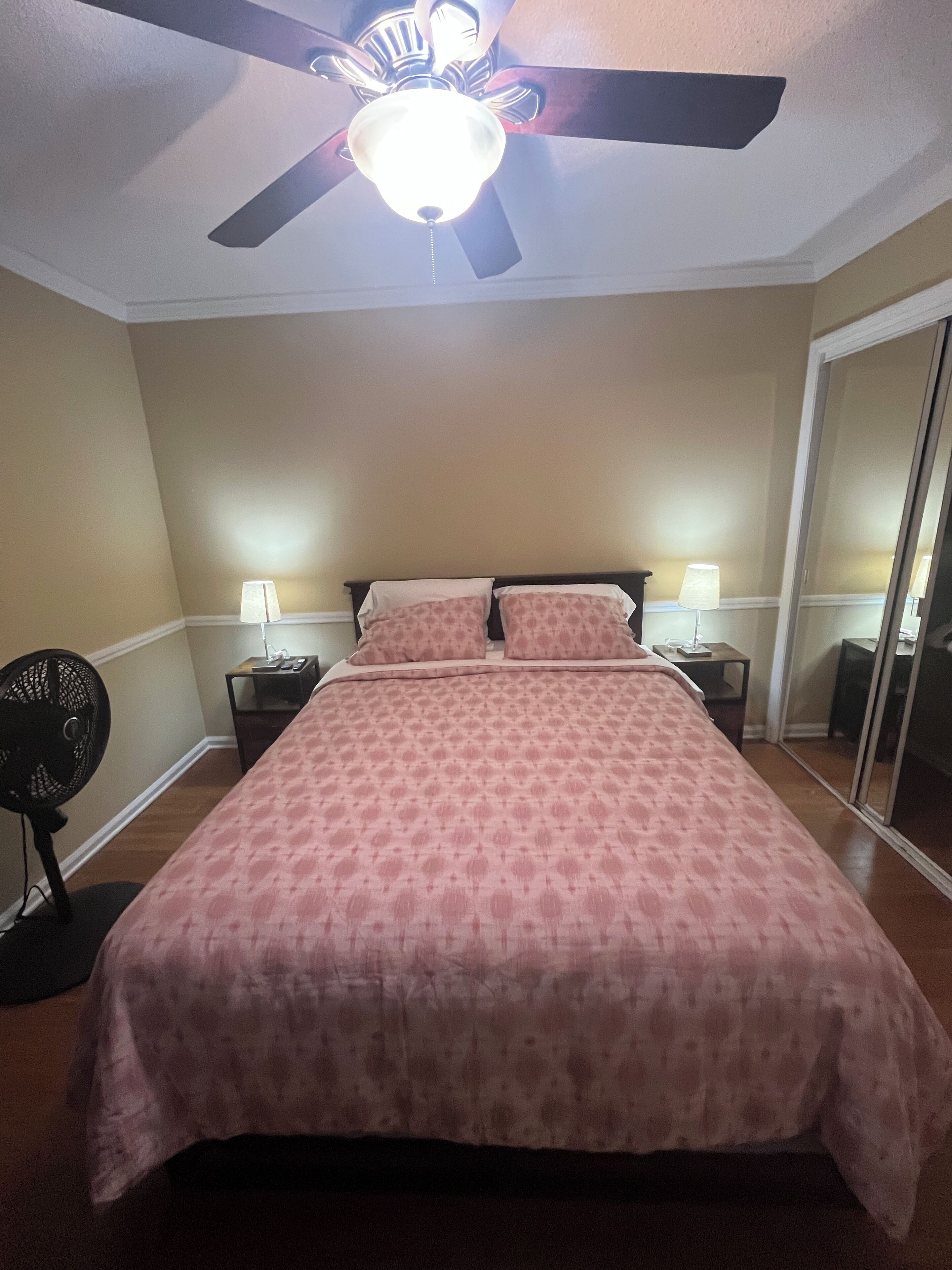 A bedroom with a bed, two bedside lamps, a ceiling fan, and a mirror.