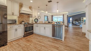 A modern kitchen with white cabinetry, stainless steel appliances, and a wooden floor. - Sleeps 6 - 3BR - 2BA - pool - Sun deck - Coastal (Cape Coral)