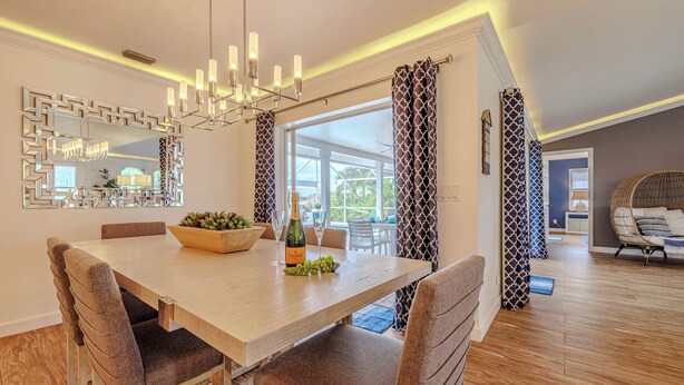 A dining area with a wooden table, upholstered chairs, a chandelier, and a large mirror. - Sleeps 6 - 3BR - 2BA - pool - Sun deck - Coastal (Cape Coral)