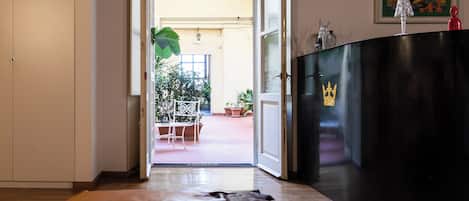 An open doorway leading to a patio with a table and chairs, a black cabinet with a crown emblem, and a painting on the wall.