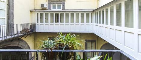 Un cortile con un balcone, piante in vaso e la facciata di un edificio con finestre e una piccola finestra sopra il balcone.