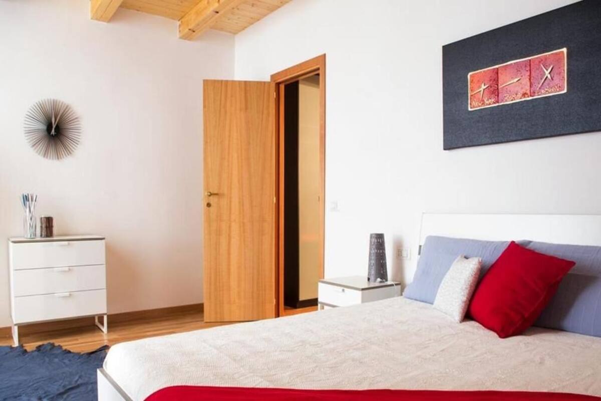A bedroom with a bed, a nightstand, a dresser, a wooden door, and a wall clock.