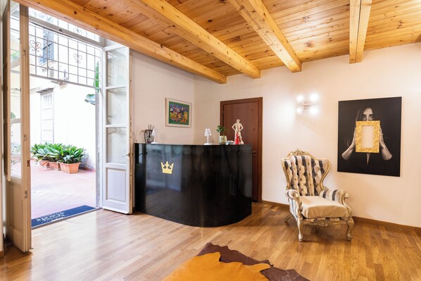 A room with a wooden ceiling, a black reception desk with a crown logo, a striped armchair, and a painting on the wall. - Residenza Principe di Carafa (Naples)