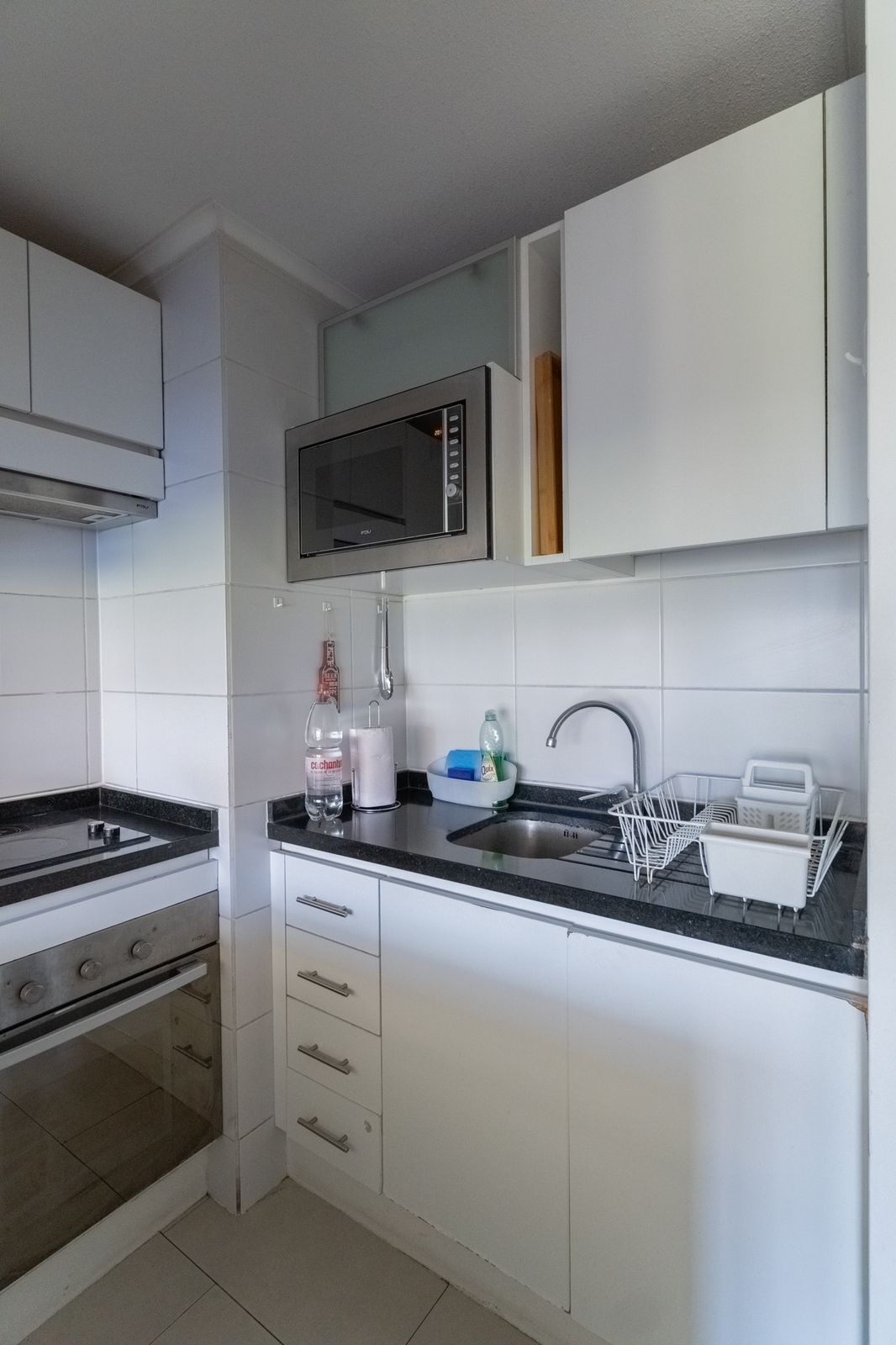 Une cuisine moderne avec des meubles blancs, un four à micro-ondes en acier inoxydable, un évier avec un égouttoir et une cuisinière à gaz.