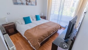 A hotel room with a bed, a TV, a heater, and a window with curtains. - Kennedy Apartments Los Militares (Santiago)