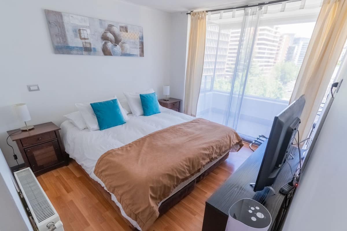 A hotel room with a bed, a TV, a heater, and a window with curtains.