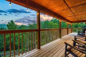 A wooden deck with a railing, overlooking a forested area.