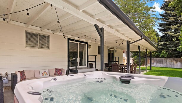 A hot tub under a covered patio with a lawn and a wooden fence in the background. - Poolside Paradise with Hot Tub (Boise)