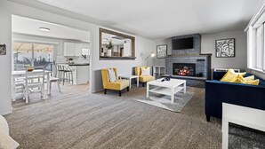 A modern living room with a fireplace, a dining area, and a kitchen visible through an open door. - Poolside Paradise with Hot Tub (Boise)