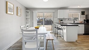 A modern kitchen with white cabinetry, a central island with bar stools, and a dining area with a white table and chairs. - Poolside Paradise with Hot Tub (Boise)