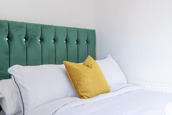 Una cama con ropa blanca y un cabecero tapizado en verde.