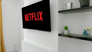 A wall-mounted TV displaying the Netflix logo in a modern room with white walls, a yellow curtain, and shelves with decorative items. - Leicester/1bedapart/petsok/tv/wifi/restaurantsnear (Leicester)