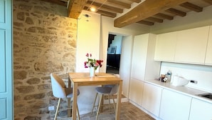 A kitchen with stone walls, wooden beams, a dining table with chairs, and white cabinets. - Villa Angela Ranza 55 (città di castello)