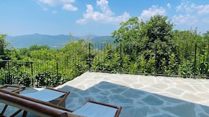 A stone-tiled terrace with bamboo furniture, surrounded by lush greenery and a clear blue sky. - Villa Angela Ranza 55 (città di castello)