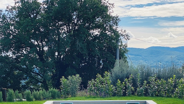 An outdoor dining setup by a pool with a table set for two, surrounded by greenery and a view of hills. - Villa Angela Ranza 55 (città di castello)
