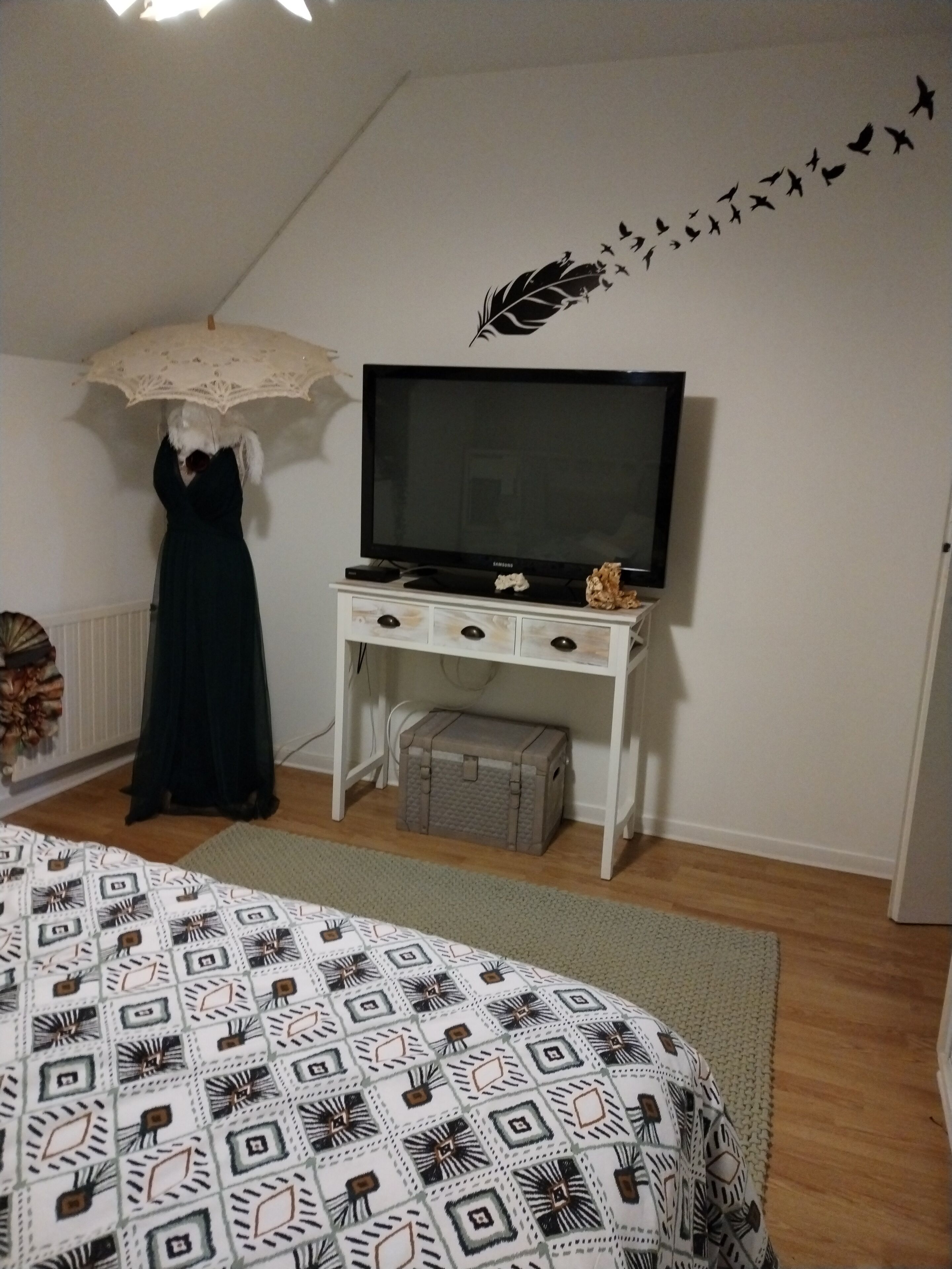 A bedroom with a bed, a TV on a white dresser, a suitcase, and a wall decal of birds.