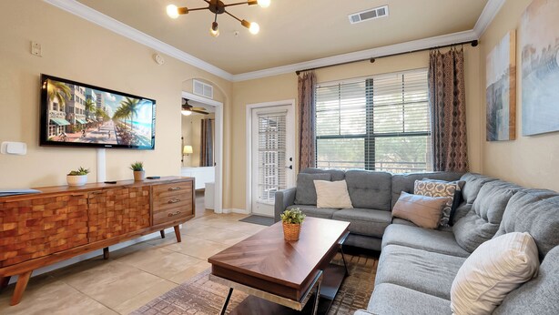 A living room with a flat-screen TV, a wooden cabinet, a grey sofa, and a coffee table. - Spacious 4 Bedroom Condo Resort Close to Disney (Davenport)