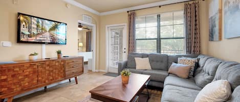 A living room with a flat-screen TV, a wooden cabinet, a grey sofa, and a coffee table.