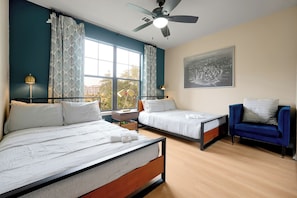 A hotel room with two beds, a ceiling fan, a window with curtains, a chair, and a wall-mounted picture.