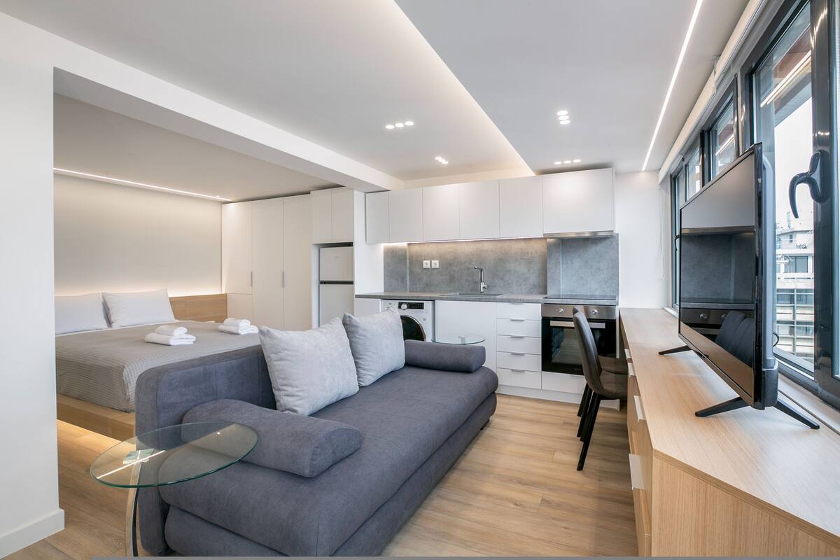 Un espace de vie moderne et compact, comprenant un coin cuisine, un canapé, une télévision et un lit.