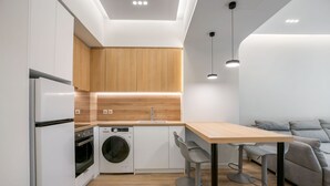 A modern kitchen with white cabinets, a wooden countertop, a built-in oven, a washing machine, and a dining area with a table and two bar stools. - Porto Pireo by Superhost365 (Piraeus)
