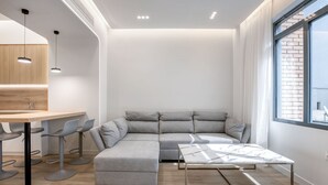 A modern living room with a sectional sofa, a dining area with bar stools, a marble coffee table, and a large window with a view of the city. - Porto Pireo by Superhost365 (Piraeus)