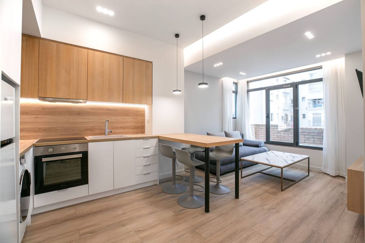 Une cuisine moderne avec des meubles en bois, un four encastré et un coin repas comprenant une table et des chaises.