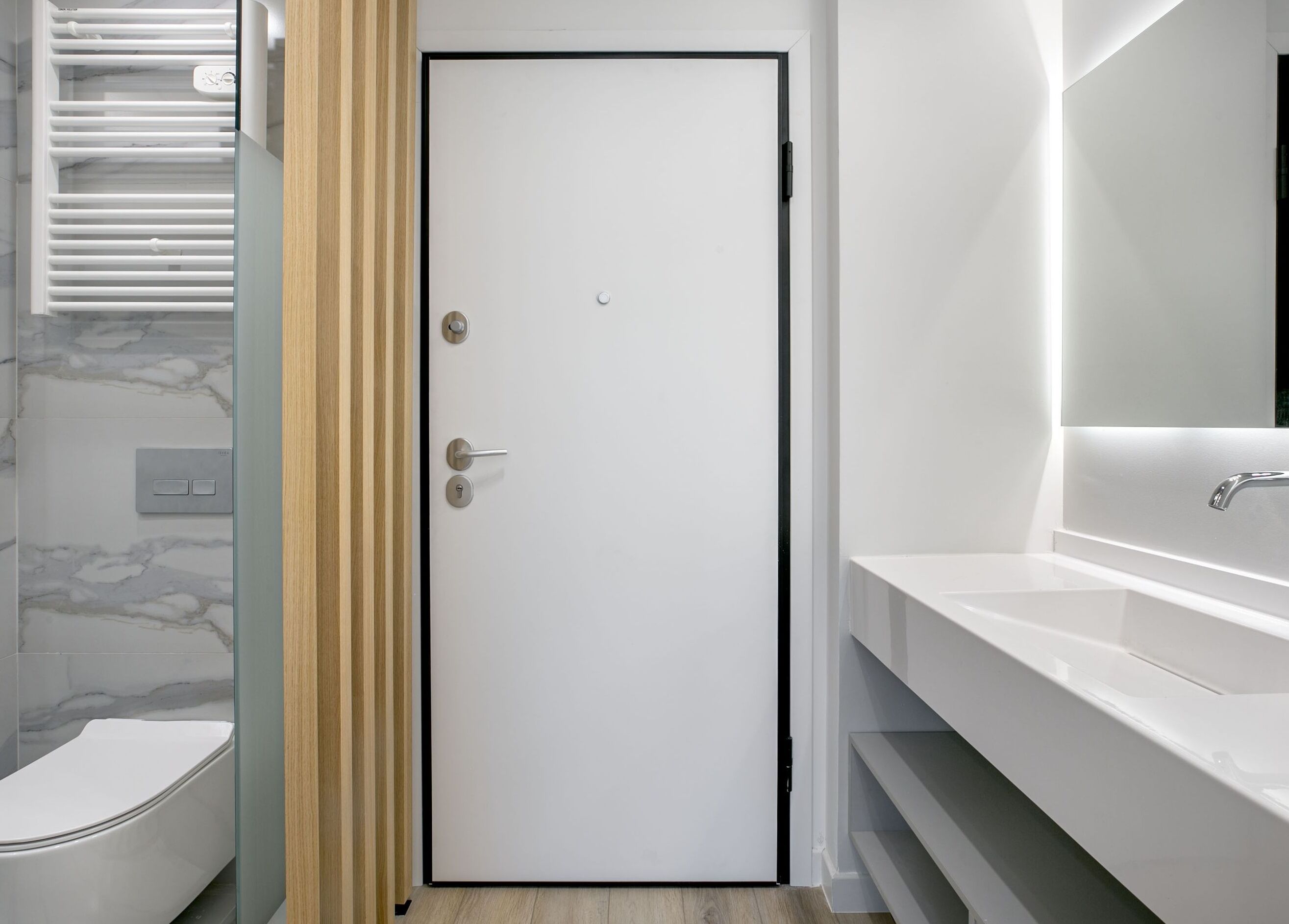 A modern bathroom with a white door, a glass shower enclosure, a white sink, and a marble backsplash.