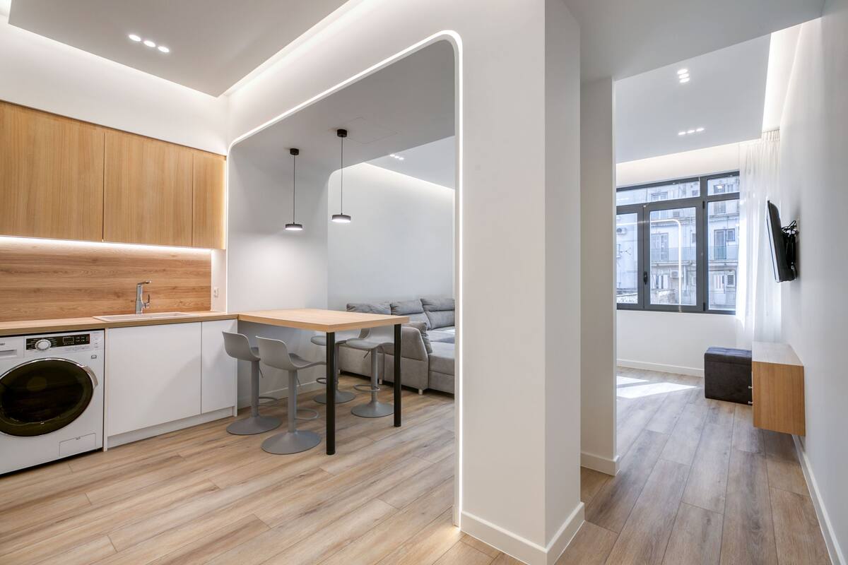 Une cuisine moderne dotée d’un plan de travail en bois, d’un lave-linge encastré et d’un coin repas avec une table et des chaises.