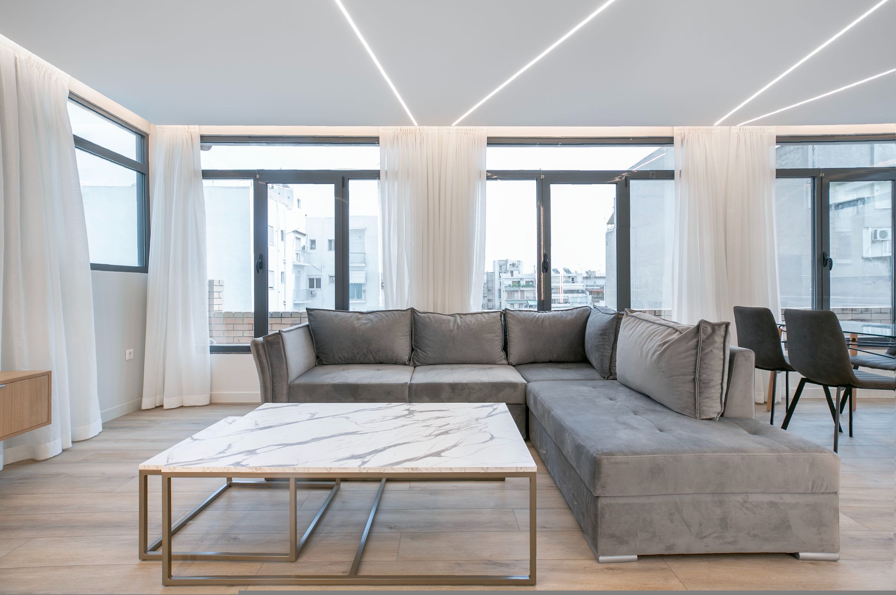 Een moderne woonkamer met een hoekbank, een marmeren salontafel en grote ramen met uitzicht op de stad.