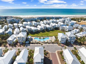 A coastal resort with multiple-story buildings, a central swimming pool, and a beach view.