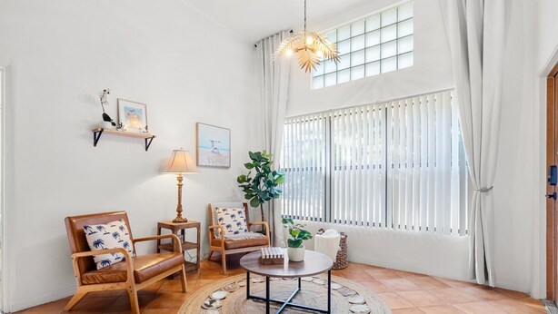 A well-lit living room with a round coffee table, two armchairs, a side table with a lamp, a potted plant, and a large window with curtains. - Casita near Madeira Beach (St. Petersburg)