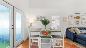 A dining area with a table set for two, a blue sofa, and a view through a glass door. - Casita near Madeira Beach (St. Petersburg)