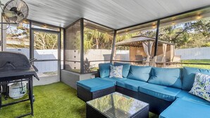 A covered patio with a blue sectional sofa, a glass-top coffee table, and a grill. - Casita near Madeira Beach (St. Petersburg)