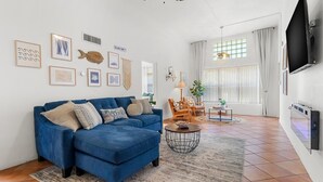 A living room with a blue sofa, a round coffee table, and a TV mounted on the wall. - Casita near Madeira Beach (St. Petersburg)