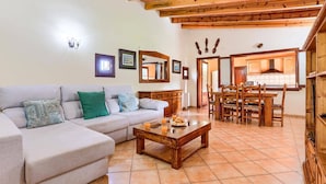 A living room with a sofa, coffee table, and dining area with wooden chairs and a kitchen in the background. - Villa Malec by Villa Plus (El Vilà)