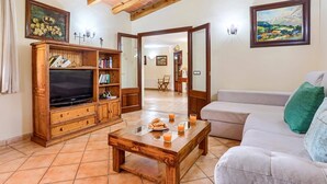 A living room with a wooden entertainment unit, a television, a sofa, and a coffee table with glasses of orange juice. - Villa Malec by Villa Plus (El Vilà)