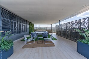 Um pátio externo com conjunto de jantar, cadeiras brancas e cerca estampada.