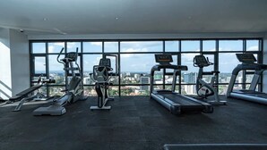 A gym with various exercise equipment, large windows, and a city view.