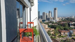 A balcony with a red chair, overlooking a cityscape with modern high-rise buildings.